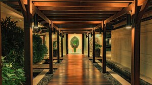 A wooden corridor with a central pathway, flanked by plants and columns, leading to a decorative area with a green wreath. - Villa Cantik Pandawa By Fays Hospitality (Kutuh)