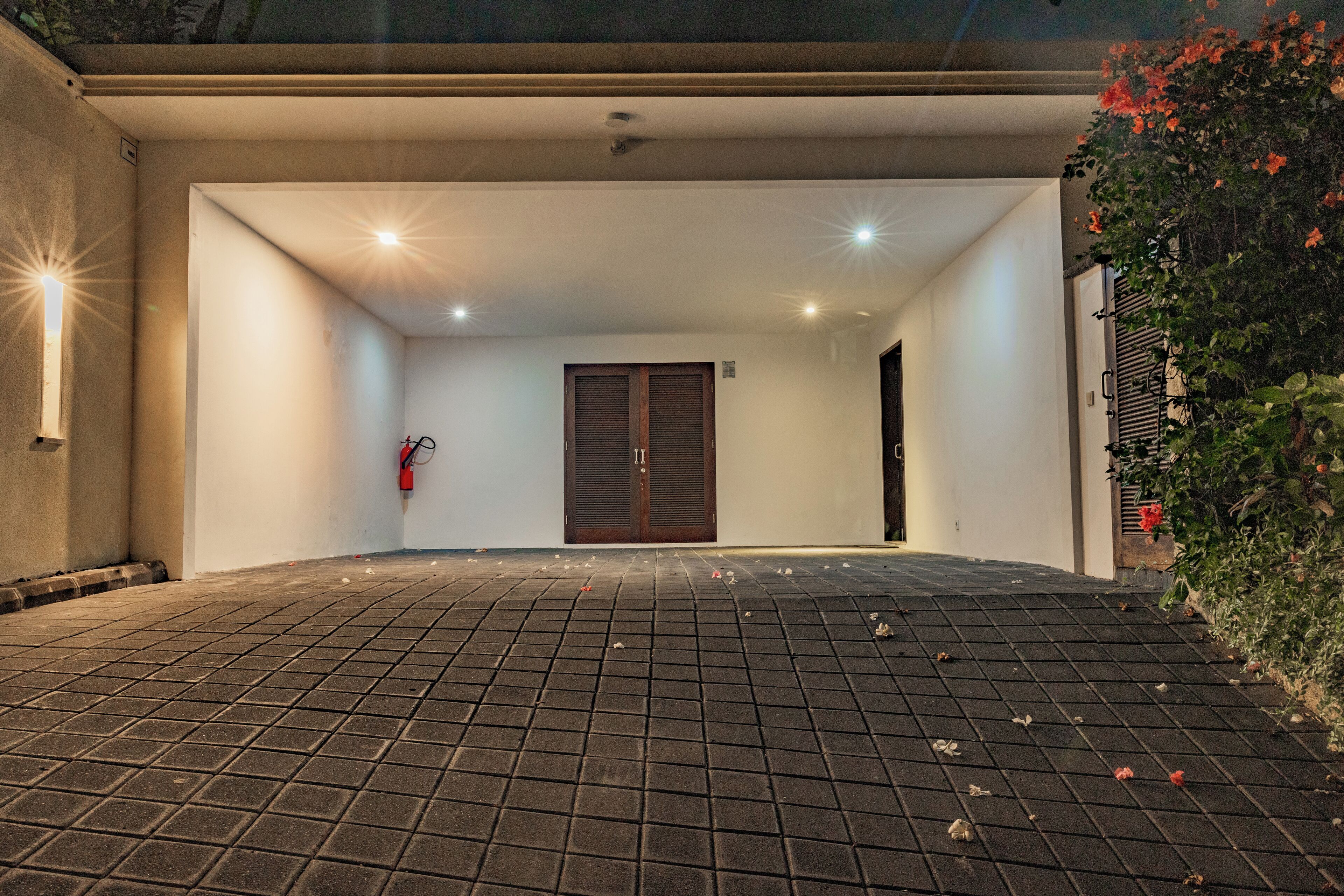 A covered driveway leading to a building with a closed door and a fire extinguisher mounted on the wall.