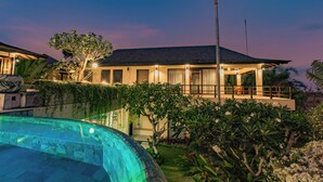 A modern house with a swimming pool, surrounded by lush greenery and a well-lit balcony. - Villa Cantik Pandawa By Fays Hospitality (Kutuh)