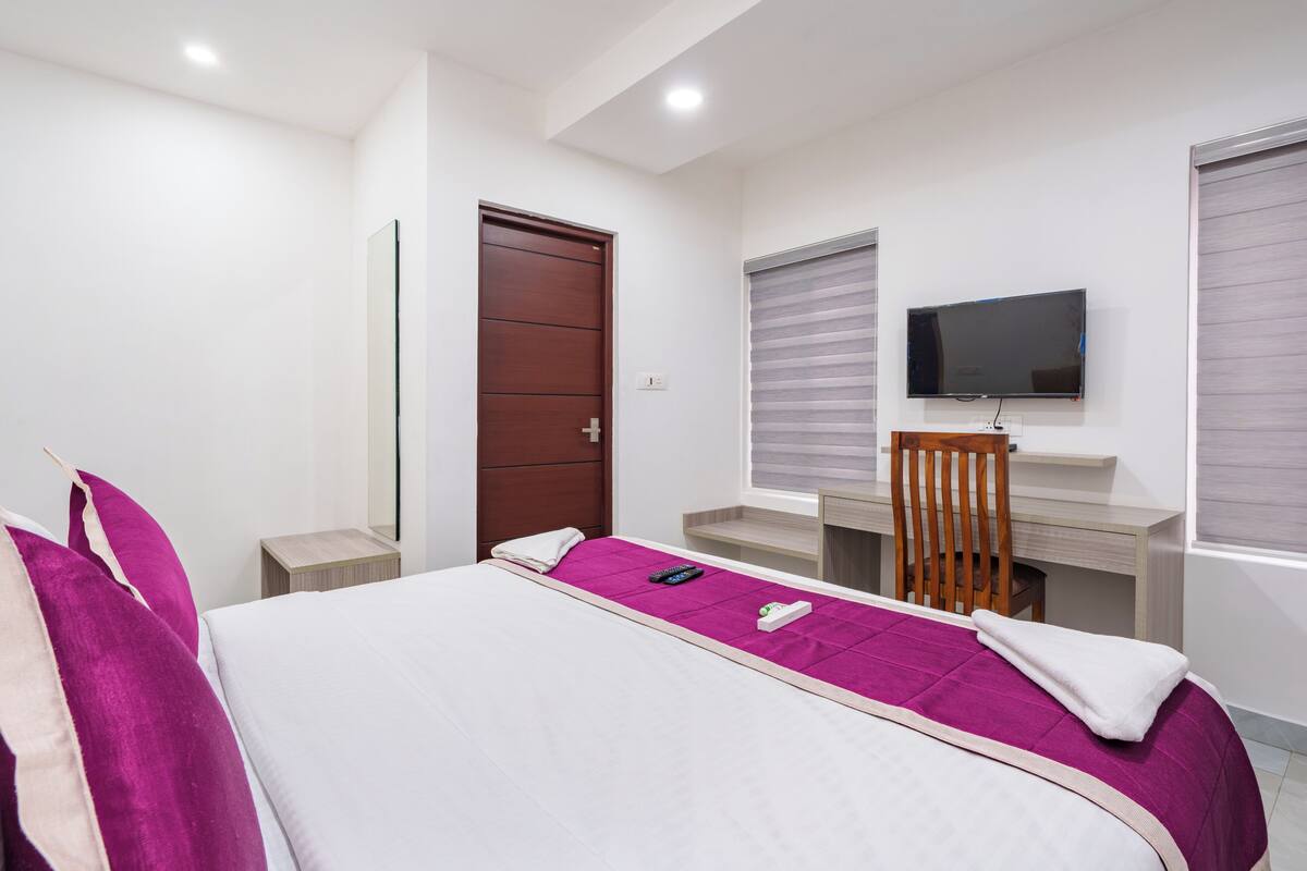 A hotel room with a bed, a desk, a chair, a TV, and a door.
