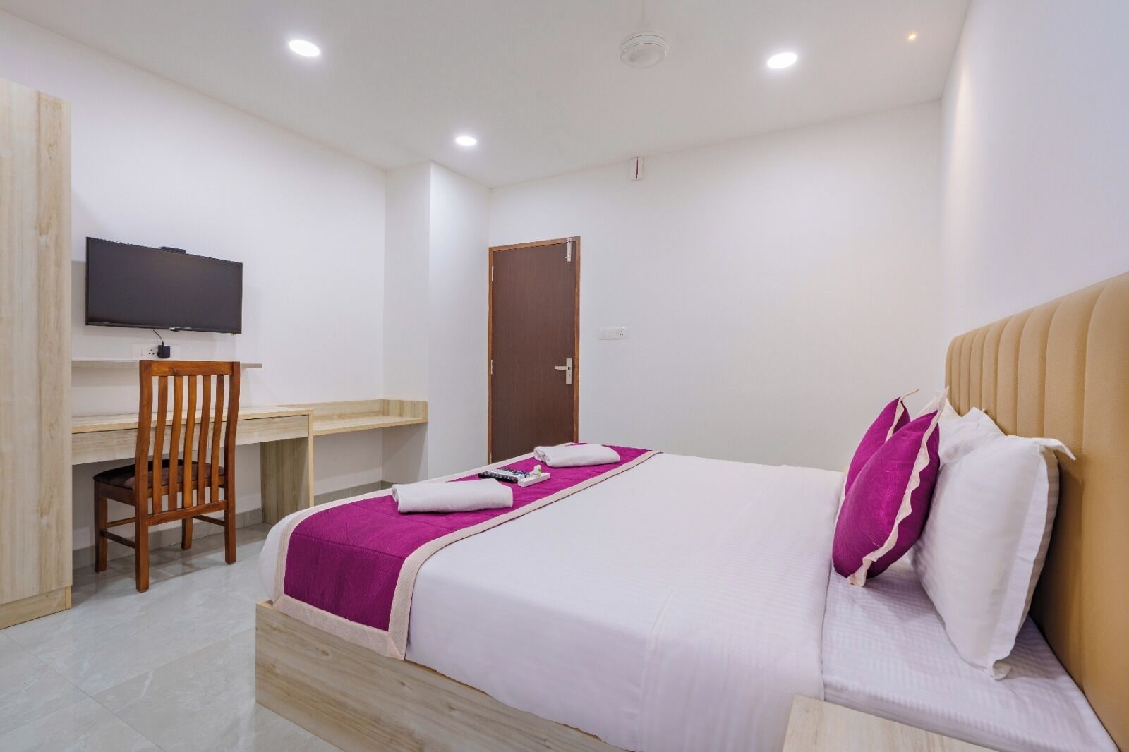 Une chambre d’hôtel avec un lit, un bureau, une chaise, une télévision et une porte.