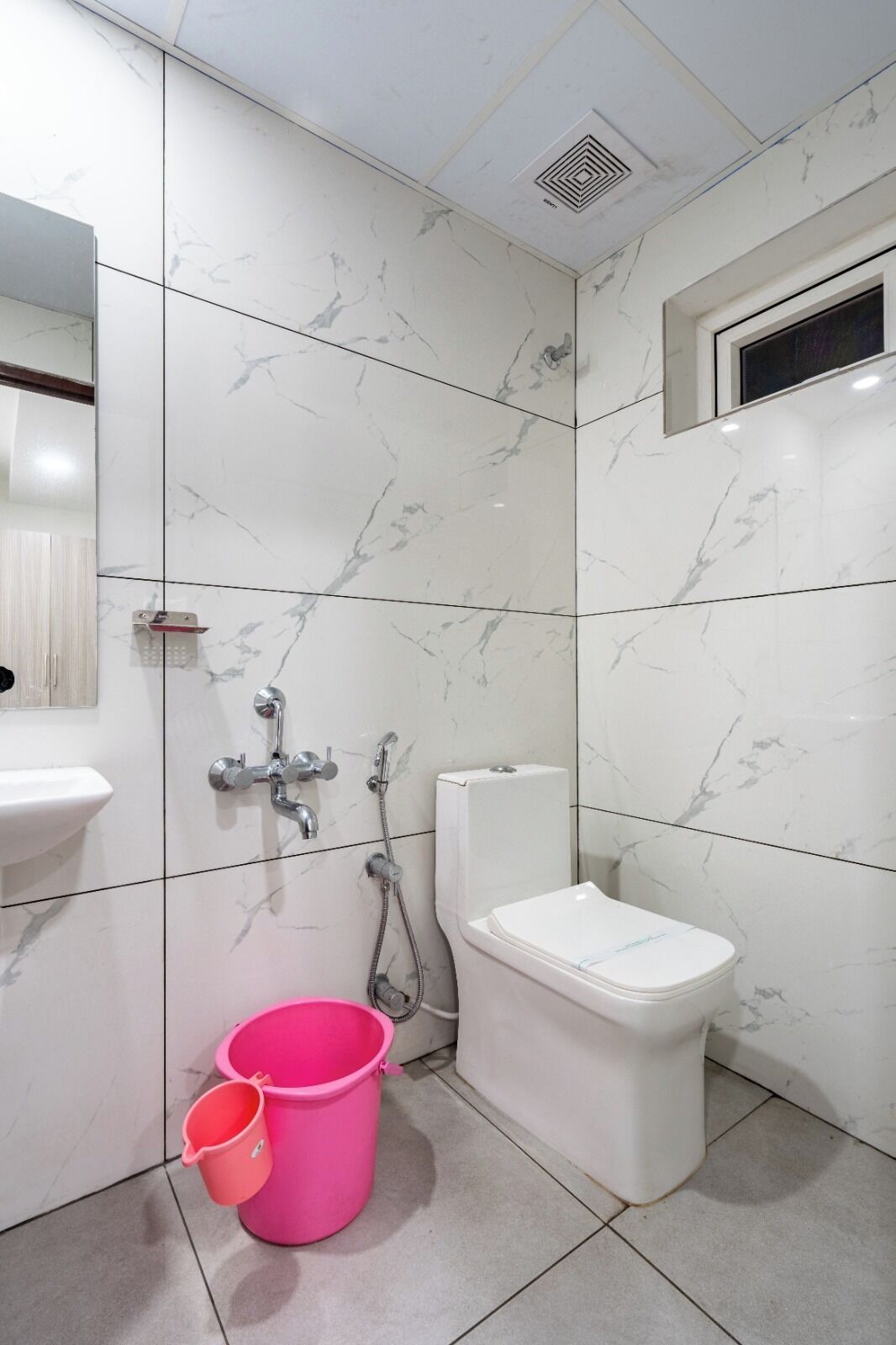 A bathroom with white marble tiles, a white toilet, a sink, and a shower.