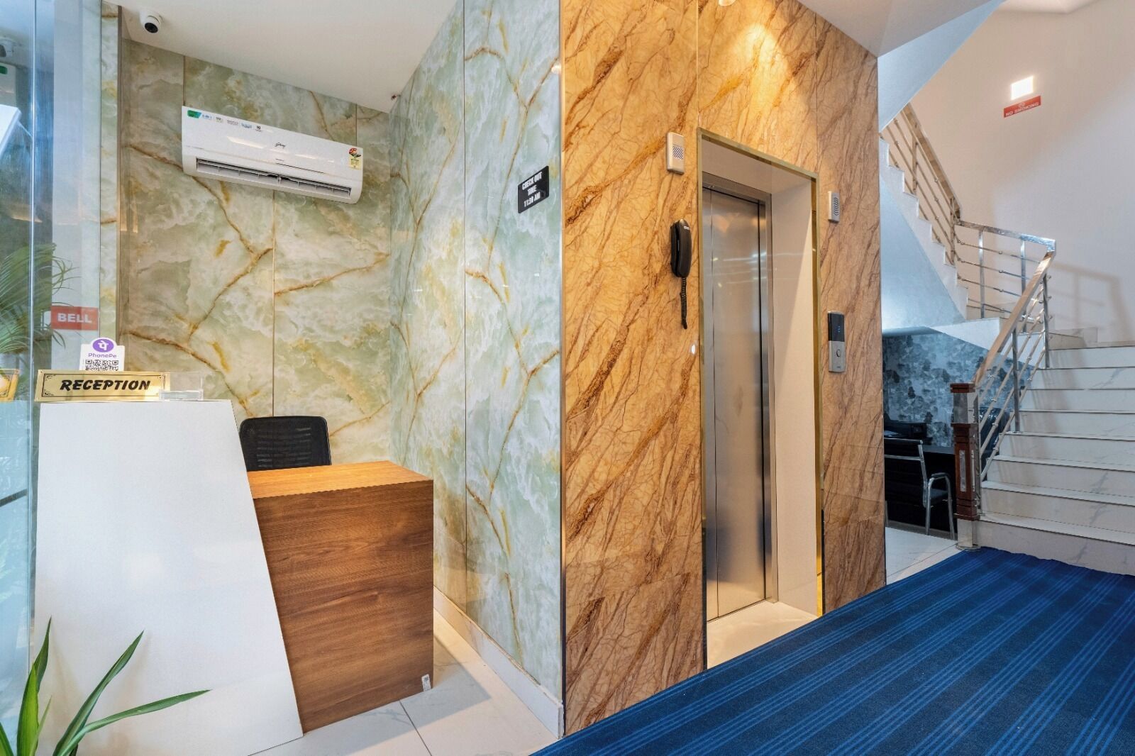 A reception area with marble walls, a reception desk, an elevator, and a staircase.