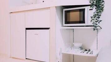 Una kitchenette compacta con microondas, una pequeña estantería con cubiertos y una puerta con manija.