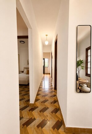 A hallway with patterned flooring, a bed, a dining area with a mirror, and a ceiling light.
