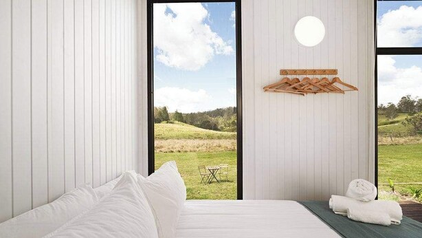 A bedroom with a large window, a bed, a towel rack, and a view of a grassy landscape.