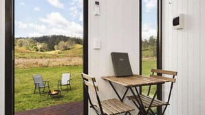 A room with a view of a grassy landscape, a small table with chairs, and a fire pit.