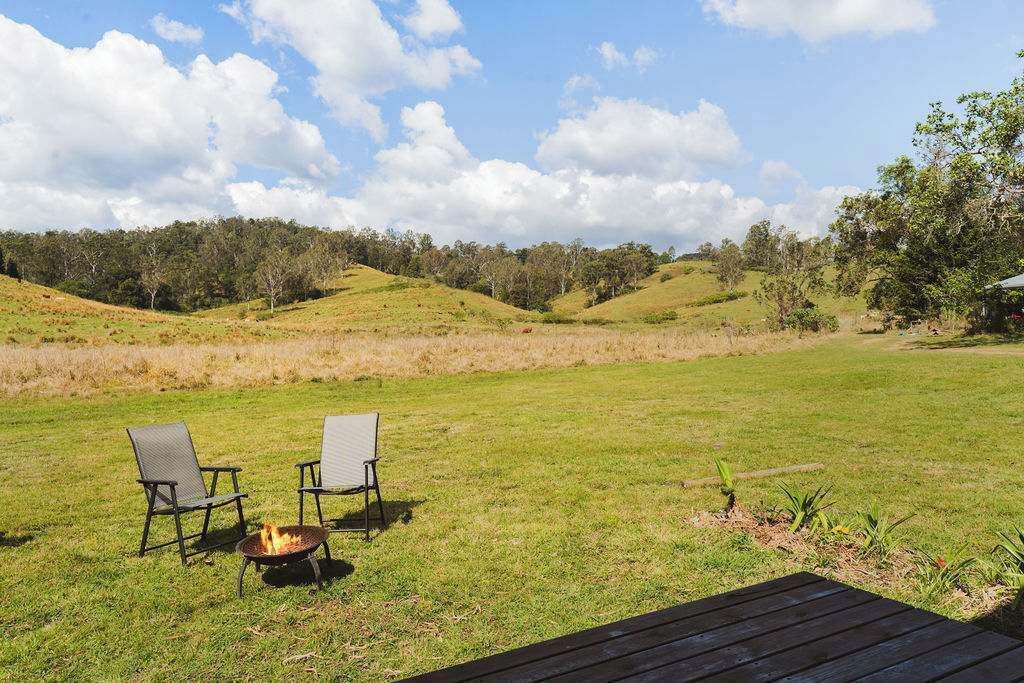 Un espacio al aire libre con césped, dos sillas y un brasero, rodeado de colinas y árboles.