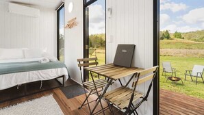 A bedroom with a bed, a desk with a laptop, and a view of the outdoors.