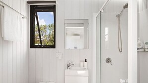 A bathroom with a toilet, sink, mirror, shower, and window.