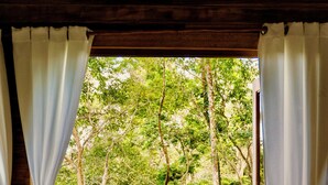 Une chambre avec un lit, des rideaux blancs et une vue sur une forêt par la fenêtre.