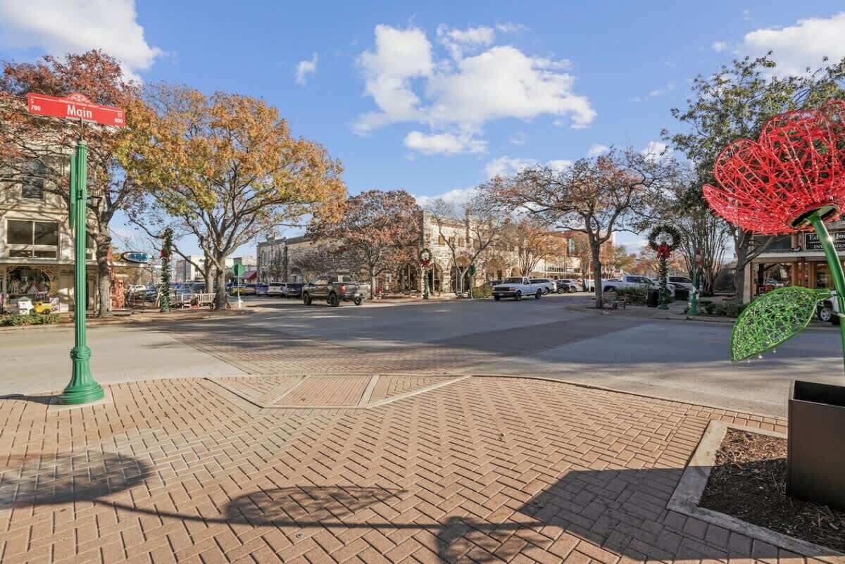 Vista d'un carrer amb vorera de maó, fanal verd i una escultura decorativa vermella i verda.