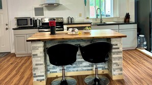 A modern kitchen with a central island, two black bar stools, a stainless steel refrigerator, and a window providing natural light. - Spacious 8-bedroom building in welcoming Fairbanks with WiFi (Fairbanks)