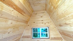 A wooden cabin room with a single bed, a small window, and a circular skylight. - Spacious 8-bedroom building in welcoming Fairbanks with WiFi (Fairbanks)