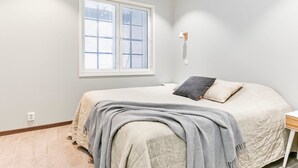 Et soveværelse med en seng, et sengebord, et vindue med persienner og en vægmonteret lampe.