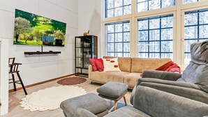 En moderne stue med et stort vindue, et fladskærms-tv, en sofa og et glashus.
