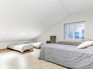A bedroom with a sloped ceiling, two single beds, a larger bed, a window with blinds, and a stone accent wall. - Levin hetki b by Interhome (Kittilä)