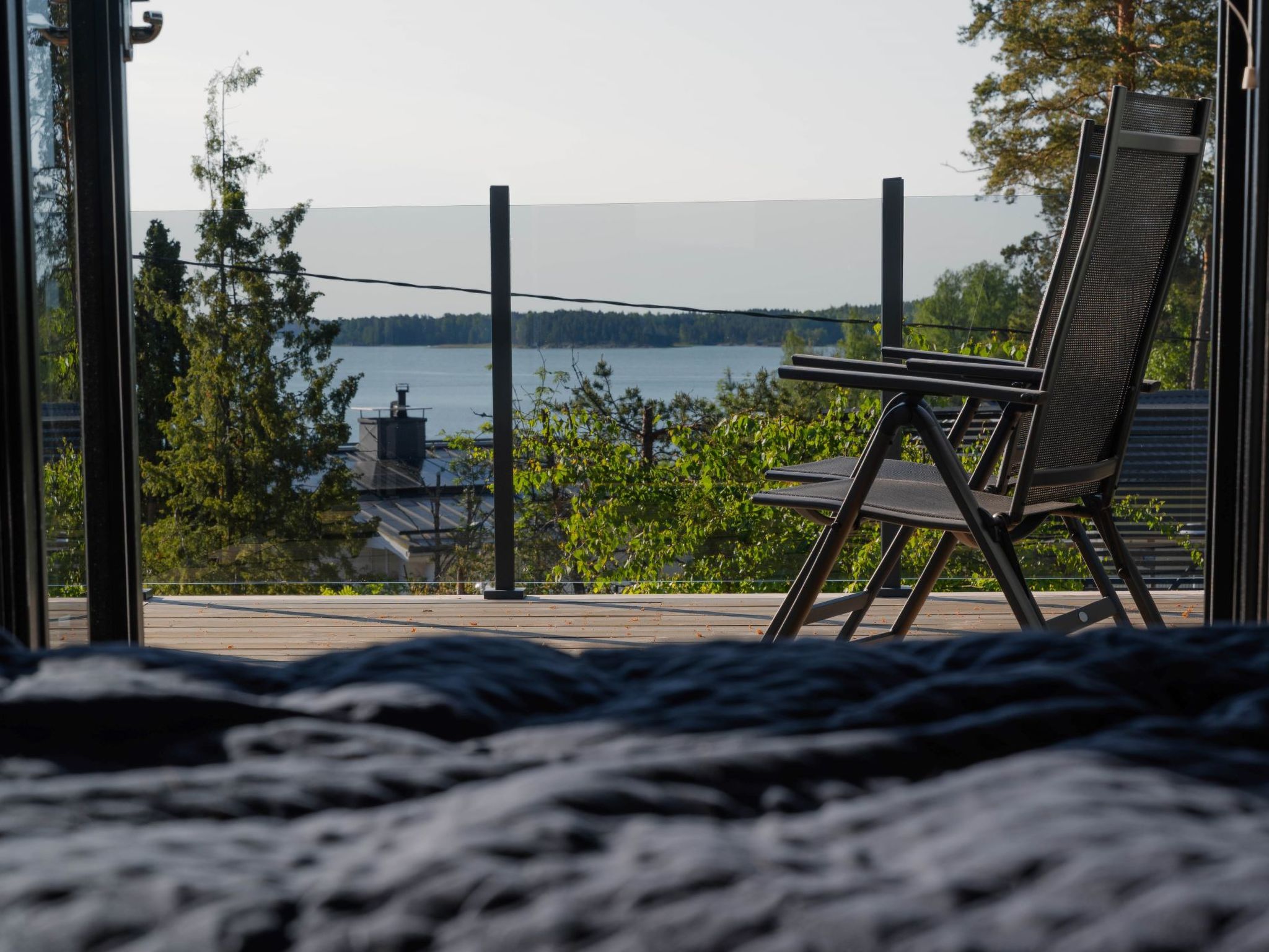 Een balkon met een stoel met uitzicht op een meer, omringd door bomen en een verre brug.