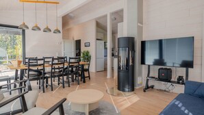 Un salon moderne comprenant un coin repas, un objet cylindrique noir, un téléviseur à écran plat et un espace dédié aux jeux vidéo.