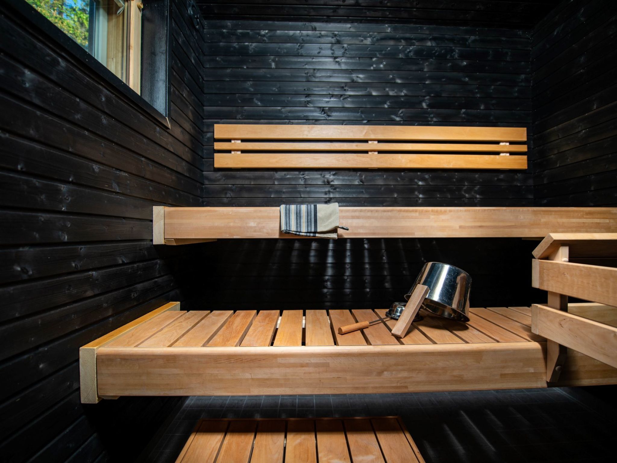 A sauna with wooden benches, a metal bucket, and a towel.