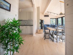 Eine moderne Küche mit weißen Schränken, einer schwarzen Arbeitsplatte und einem Spülbecken. Ein Essbereich mit Holztisch und Stühlen lädt zum Verweilen ein. Ein großes Fenster sorgt für natürliches Licht und Blick ins Freie.