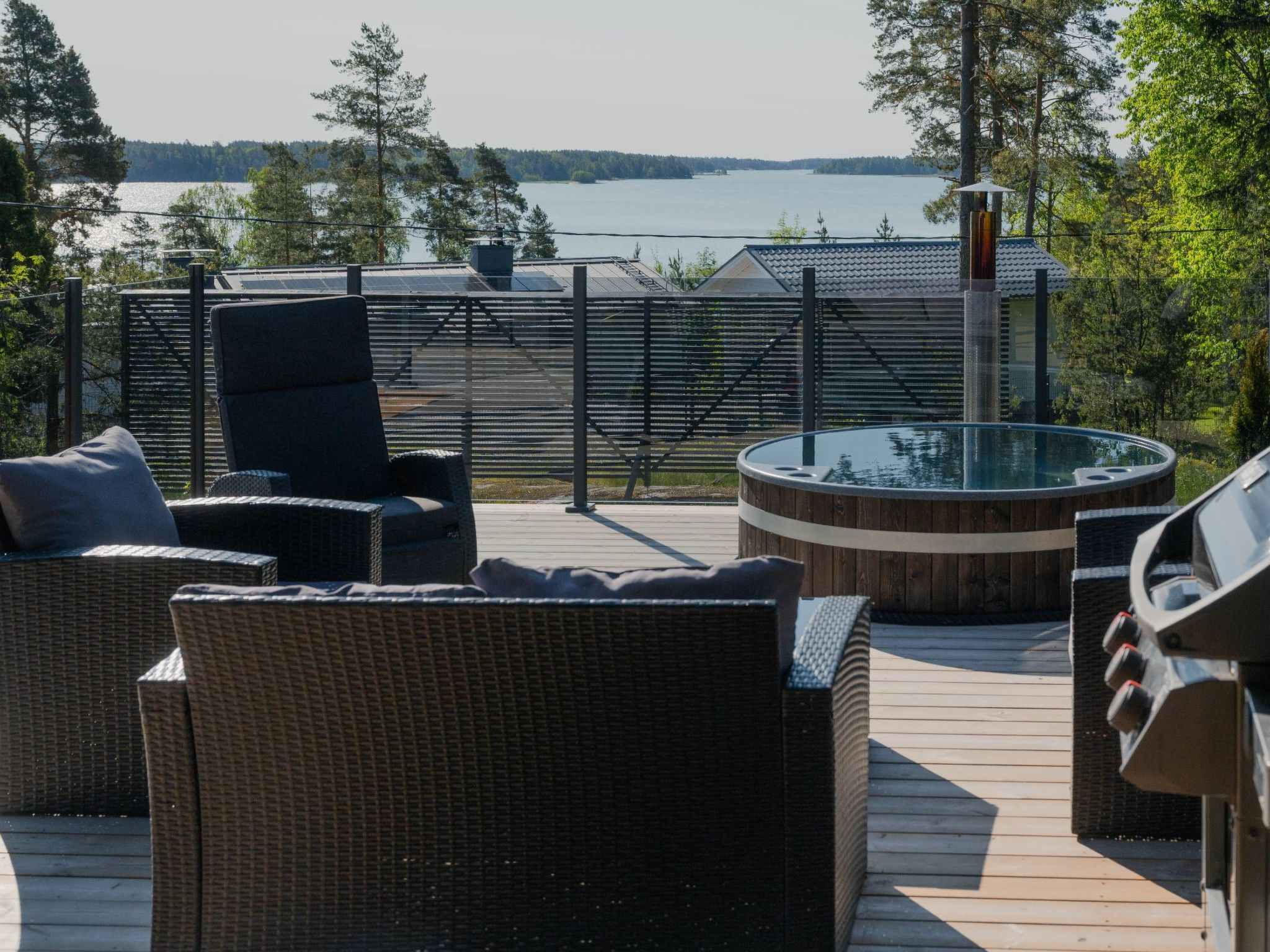 A deck with wicker furniture and a hot tub overlooking a lake.