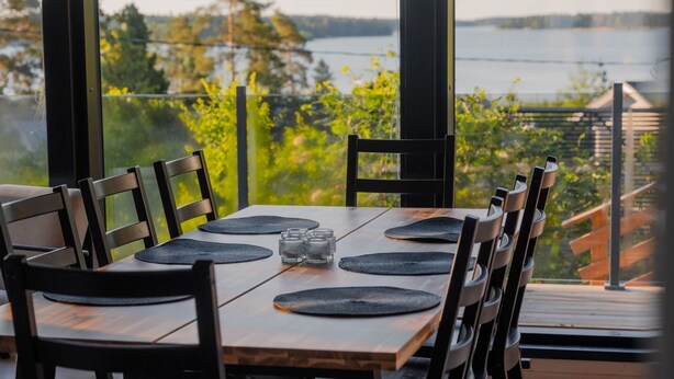 Un coin repas avec vue sur un lac, une table en bois, des chaises et des sets de table noirs.