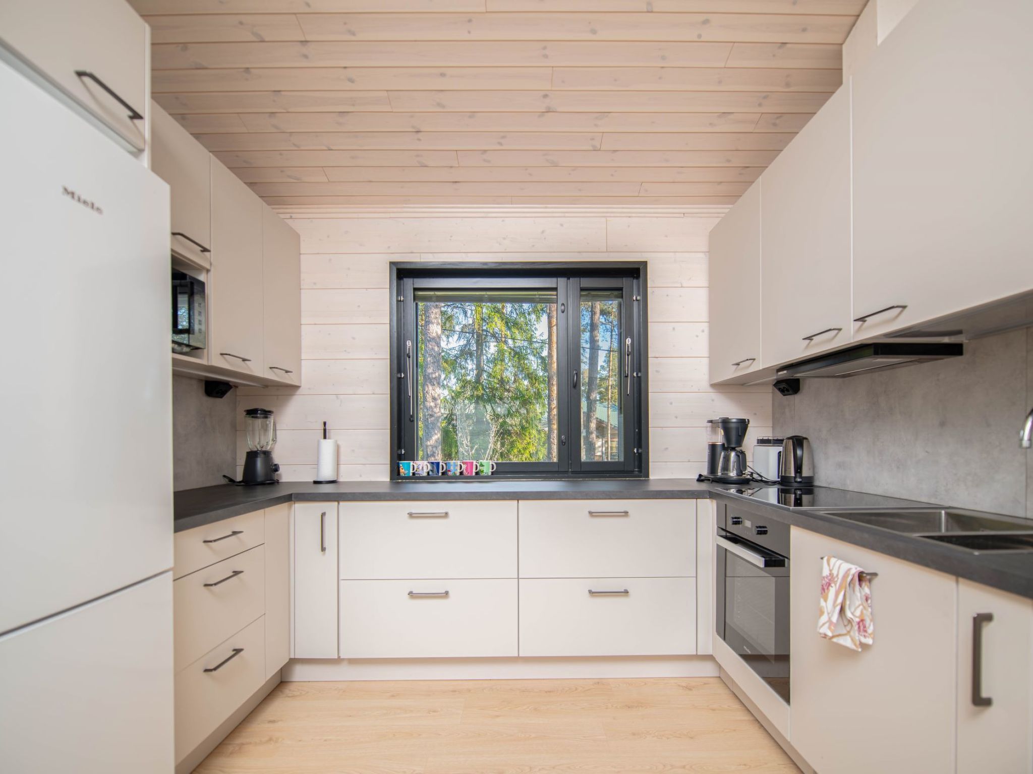 Een moderne keuken met witte kastjes, een zwart aanrecht en een raam met uitzicht op bomen.