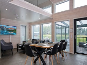 A spacious room with a large dining table, black chairs, and a view of the outdoors through large windows.