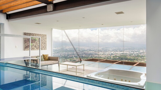 A modern infinity pool with a city view, a sun lounger, and a hot tub.