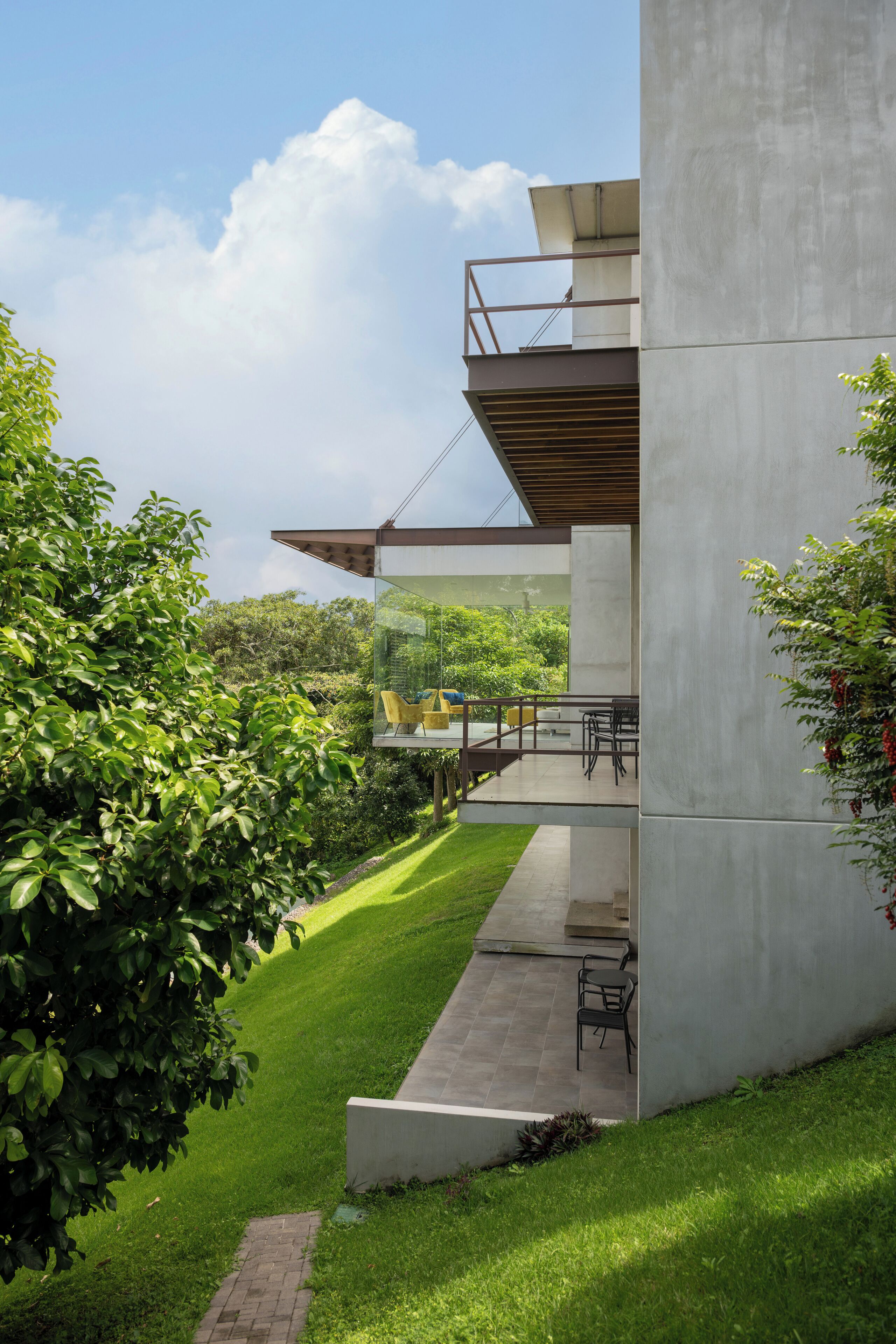 A modern building with a glass balcony, outdoor seating, and a well-maintained lawn.