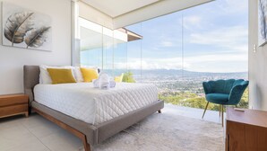 A modern bedroom with a large bed, a view of a cityscape, and a blue chair.