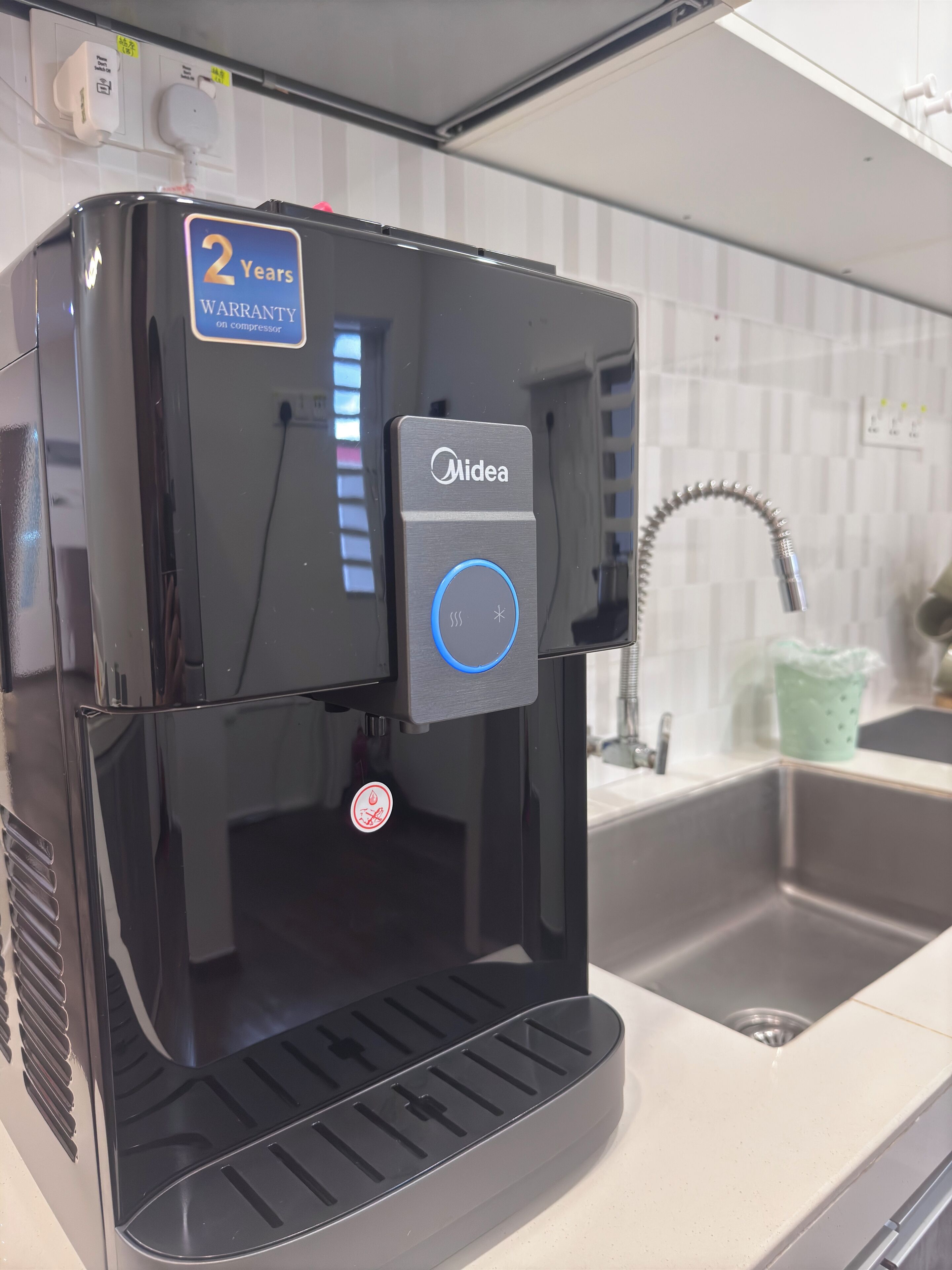 Eine Küche mit einer Kaffeemaschine der Marke 'Midea' und einem Etikett mit '2 Years Warranty'.
