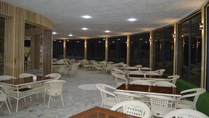 Un espace de restauration intérieur avec des tables et des chaises, de grandes fenêtres et un plafond doté d’un éclairage encastré.
