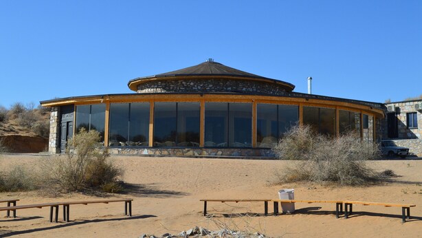 Un bâtiment circulaire doté de grandes fenêtres et d’une façade en pierre, situé dans un environnement désertique.