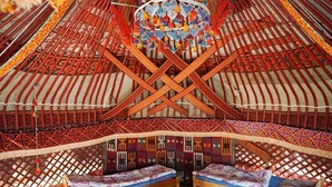 Une yourte traditionnelle, dotée d’un toit orné de motifs, d’une structure de support centrale et de deux bancs avec des coussins.