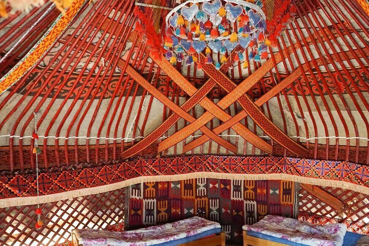 Une yourte traditionnelle, dotée d’un toit orné de motifs, d’une structure de support centrale et de deux bancs avec des coussins.