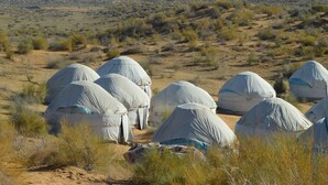 Un paysage désertique avec plusieurs structures abritées, vraisemblablement des tentes, disposées en rangée.