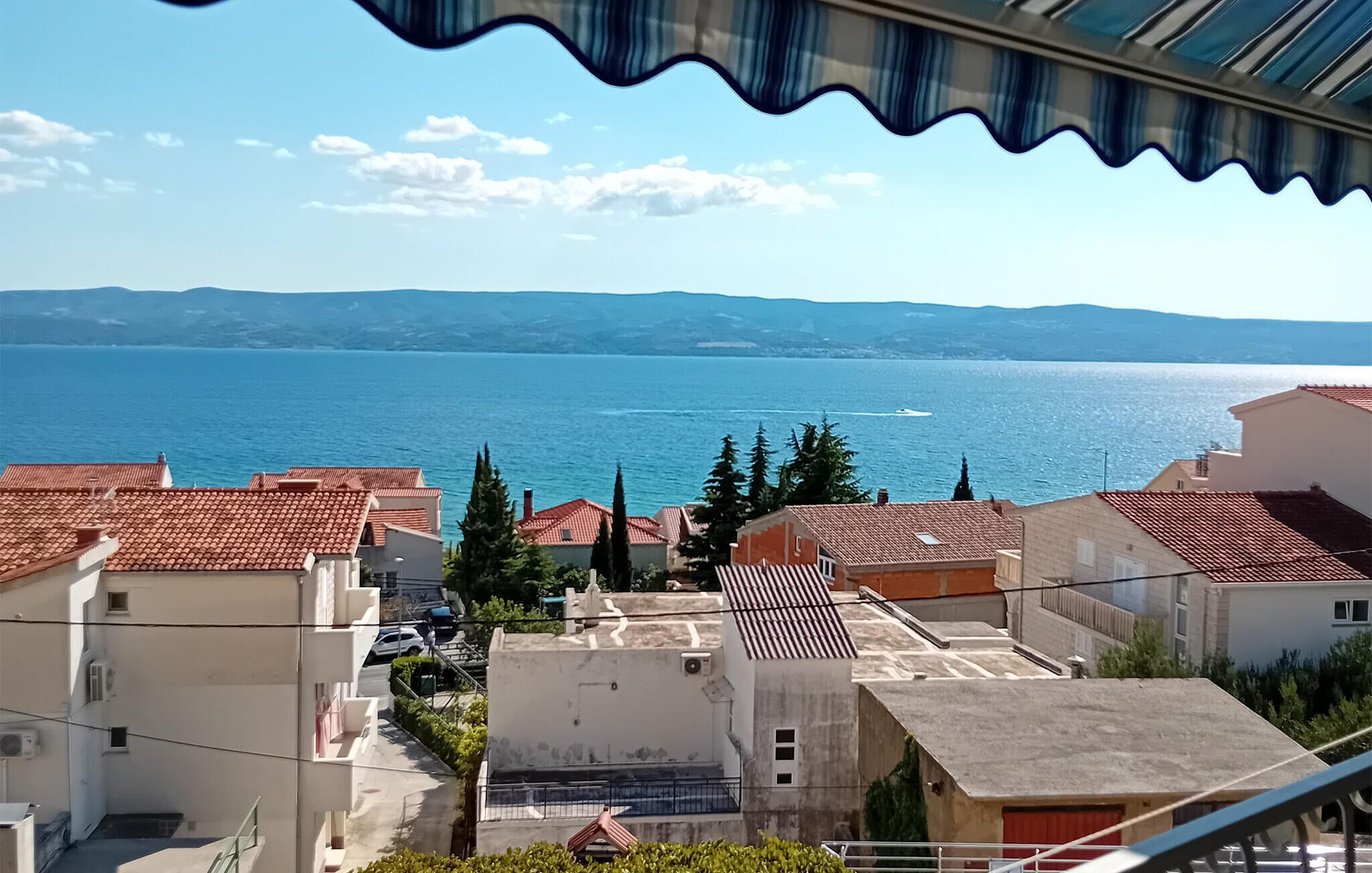 Un quartier résidentiel situé sur la côte, avec des bâtiments aux toits de tuiles rouges, une vue dégagée sur la mer et des montagnes à l’horizon.