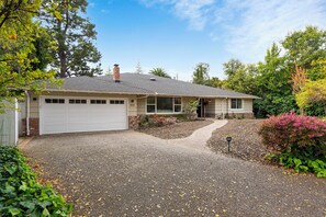 Einbungalow mit Garage, umgeben von Bäumen und Sträuchern.
