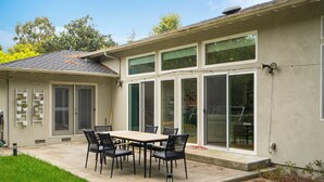 A patio with a table and chairs, a small garden, and a house with large windows and a garage.