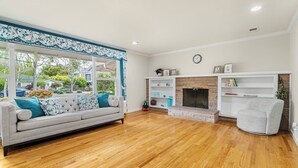 A living room with a grey sofa, wooden flooring, a fireplace, and a view of the outside.
