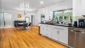 A modern kitchen with white cabinets, stainless steel appliances, and a wooden floor.