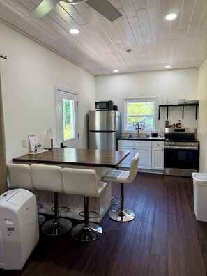 A modern kitchen with a wooden island, bar stools, stainless steel appliances, and a window with a view of greenery. - 2BR Tiny House - Hot Tub – Near Salmon River (Pulaski)