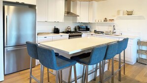 A modern kitchen with white cabinets, stainless steel appliances, and a central island with bar stools. - Spacious 3-bedroom/ 2 bath apartment in Topanga Hills with AC (Topanga)
