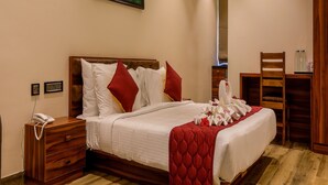 A neatly made bed with white bedding and red pillows, a wooden bedside table with a phone, and a wooden chair in a room with wooden flooring and a wooden headboard.
