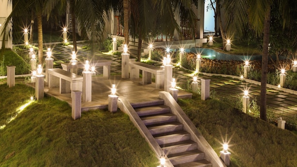 A well-lit outdoor area with a stone pathway leading to a seating area, surrounded by palm trees and illuminated by numerous lights.