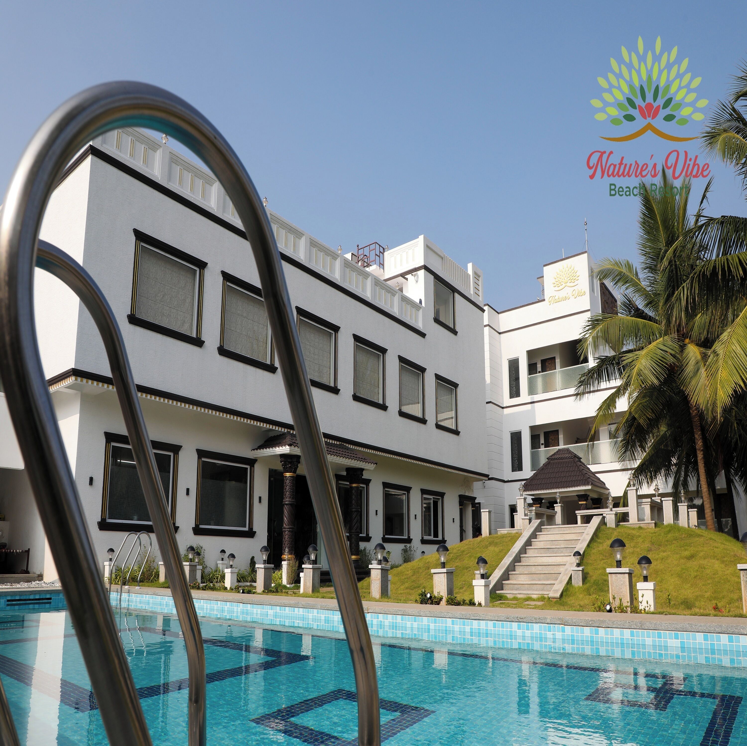 Um hotel moderno com piscina, uma escadaria que leva à entrada e uma placa para Nature's Vibe Beach Resort.