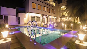A modern resort building with a swimming pool, illuminated by decorative lighting.