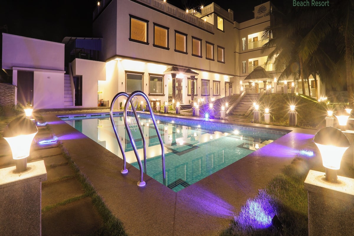Un bâtiment moderne abritant un complexe hôtelier, doté d’une piscine illuminée par un éclairage décoratif.